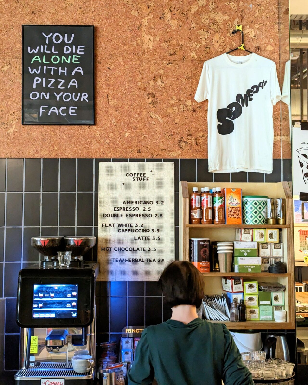 Coffee counter at Someday with the coffee menu, Someday t-shirt and pizza sign