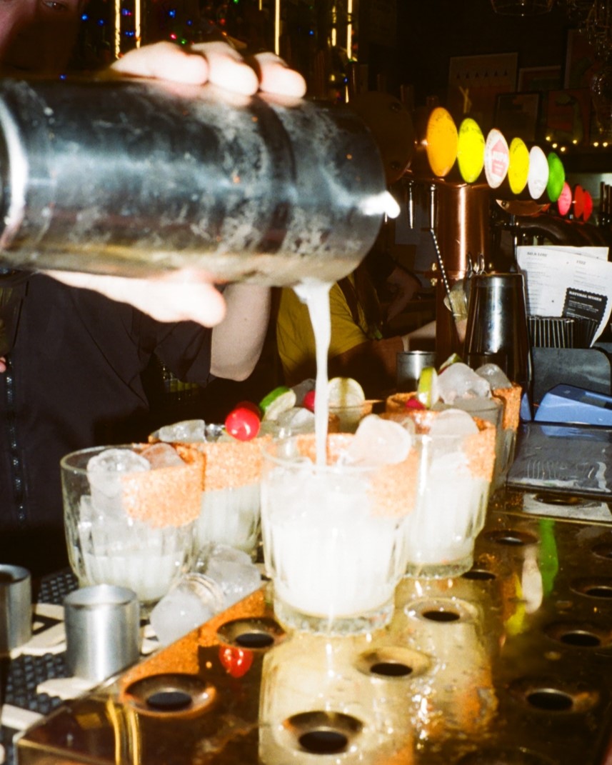 Photo of two rows of margarita glasses with margarita being poured into them.